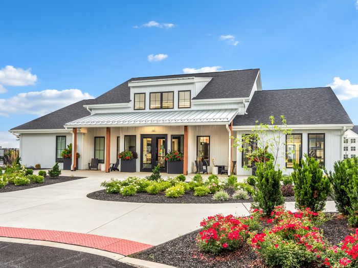 Charming white house with beautiful landscaping, featuring a spacious porch and modern design elements under a vibrant blue sky.