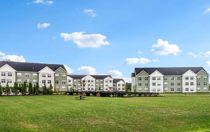 Charming apartment complex with modern architecture, lush green lawns, and picturesque skies setting a serene atmosphere.