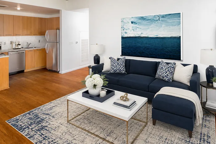 Elegant living space with navy blue sofa and modern kitchen, featuring sleek stainless steel appliances and stylish decor.