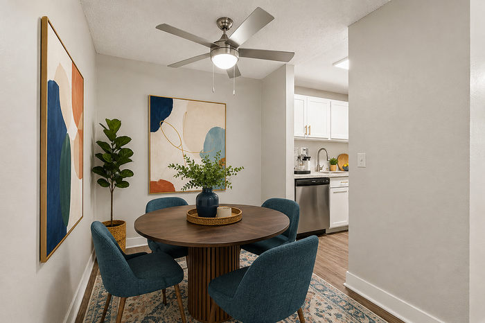 Chic dining area with modern table, cozy blue chairs, vibrant abstract art, and a glimpse of a sleek kitchen.