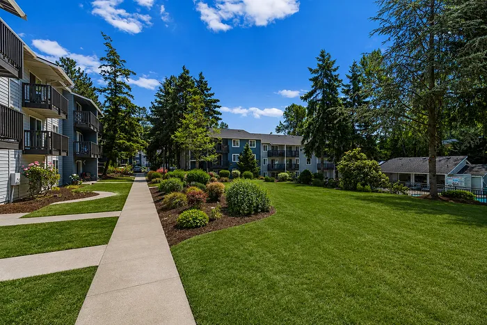 Charming apartment community with lush landscaped gardens and a sunny pathway leading to elegant multi-story buildings.