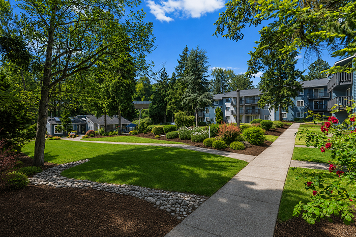 Charming apartment complex surrounded by lush, landscaped gardens and vibrant greenery under a clear blue sky.