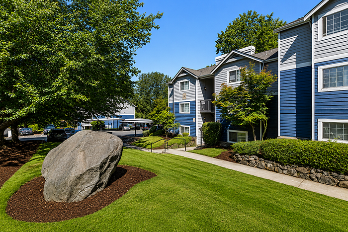 Charming apartment complex with lush landscaping and vibrant blue exterior, featuring a serene garden and welcoming pathways.