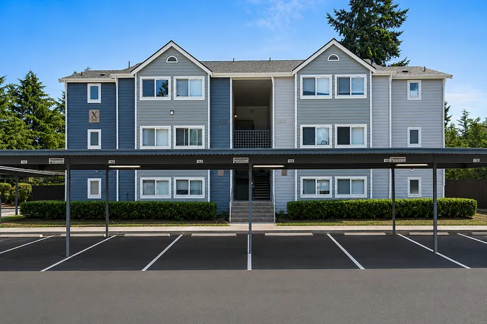 Charming modern apartment building with a stylish blue facade, framed by lush greenery and ample parking.