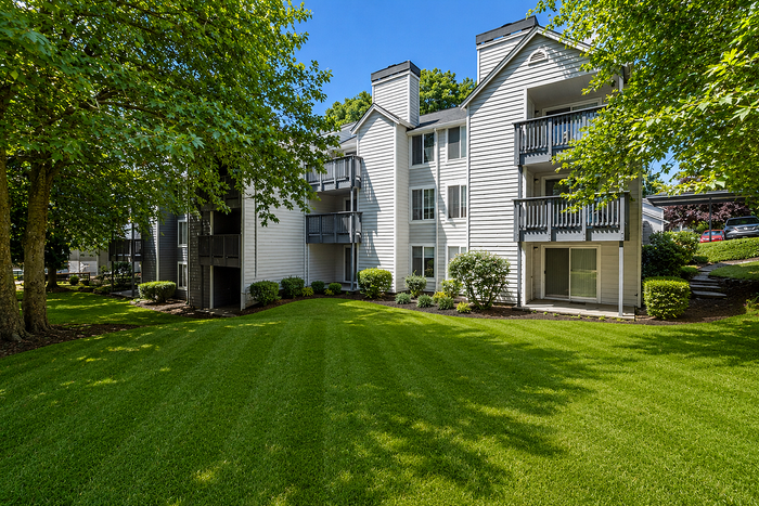 Charming apartment exterior with crisp white siding, spacious balconies, and lush greenery, offering serene and inviting surroundings.