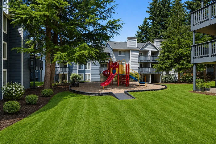 Charming apartment complex surrounded by lush greenery, featuring a colorful playground for an ideal family-friendly environment.