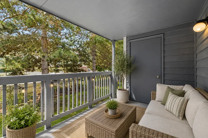Charming covered balcony with cozy seating, surrounded by lush greenery and elegant lighting.