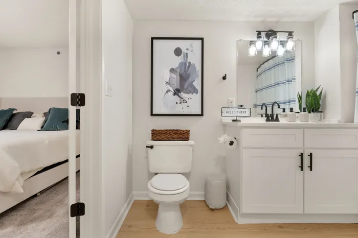 Chic bathroom with modern vanity, stylish artwork, and inviting doorway view to a cozy bedroom.