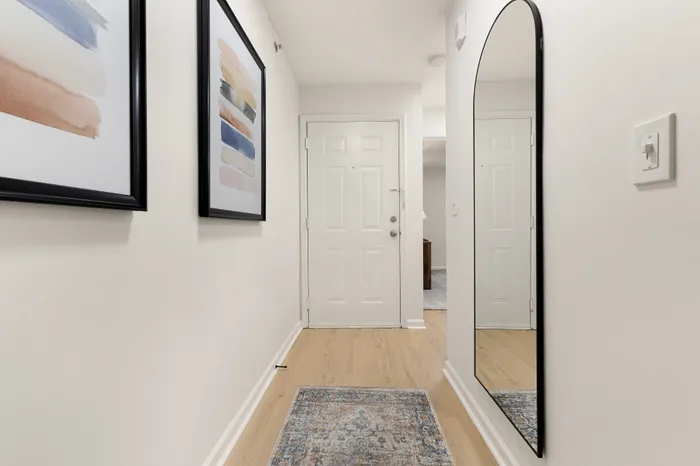 Bright and inviting hallway with sleek wooden flooring, modern abstract art, and a large elegant mirror enhancing the space.