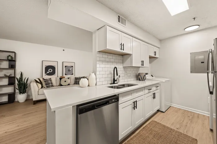 Modern apartment showcasing a sleek kitchen with white cabinetry and stainless steel appliances, adjacent to a cozy living area with stylish decor.