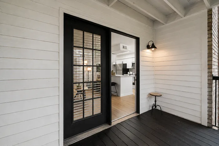 Charming porch entrance with a modern glass door leading into a cozy, well-lit interior and a sleek kitchen area.