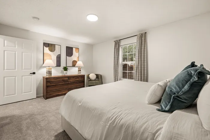 Elegant modern bedroom with soft lighting, featuring a cozy bed with plush pillows, stylish artwork, and a large window allowing natural light to enhance the serene ambiance.