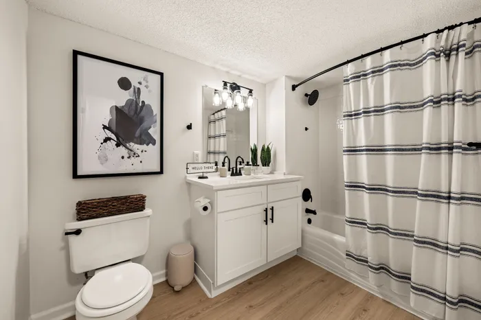 Chic bathroom with modern fixtures, stylish abstract art, and elegant striped shower curtain, showcasing a sophisticated and welcoming ambiance.