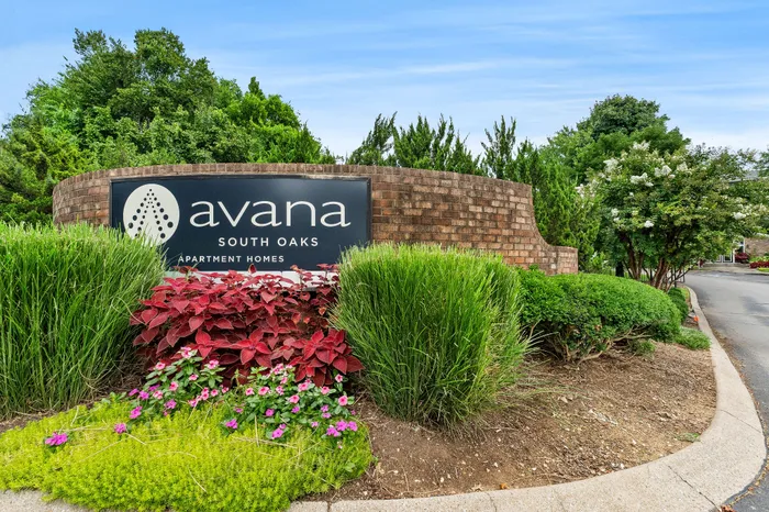 Welcoming sign for Avana South Oaks Apartment Homes surrounded by lush landscaping and vibrant flowers.