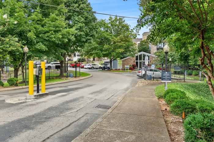 Inviting entrance to a modern apartment complex with lush greenery and ample parking.