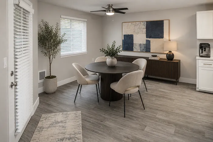 Elegant dining area featuring a round table with stylish chairs, modern art, and lush greenery, complemented by sleek wood flooring and contemporary lighting.