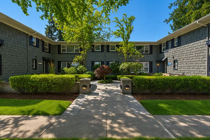 Charming apartment complex with elegant exterior, lush greenery, and inviting pathway under sunny skies.