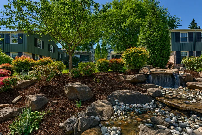 Lush apartment garden featuring vibrant landscaping, a tranquil waterfall, and serene green surroundings.