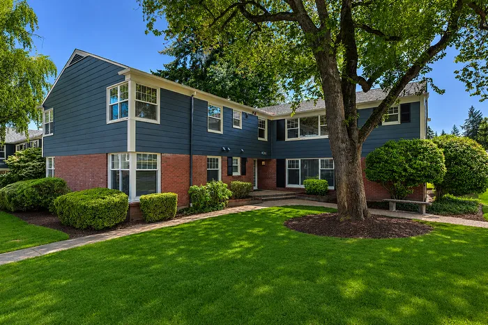 Charming two-story apartment building with classic brick and siding exterior, nestled in lush greenery and mature trees.