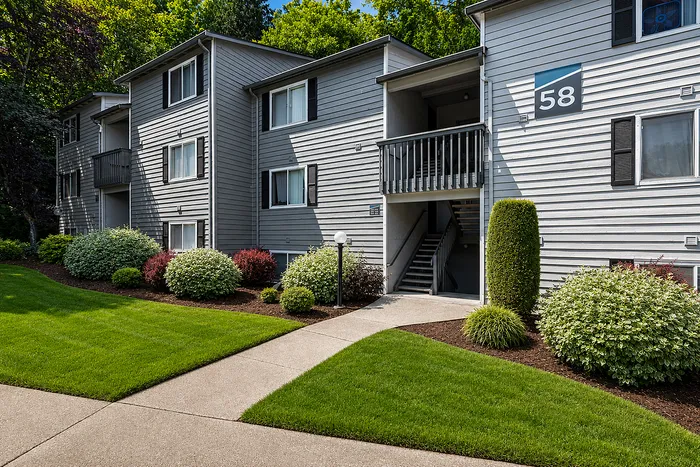 Charming apartment building with modern gray exterior, lush landscaping, and inviting pathways.