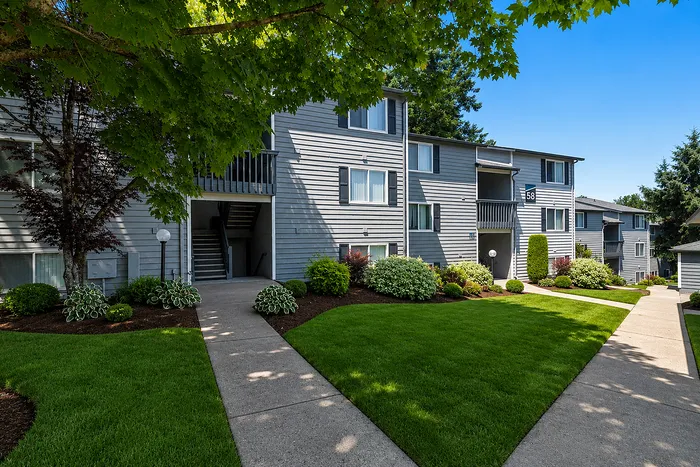 Charming apartment exterior with manicured gardens and inviting walkways, set beneath lush, green trees.