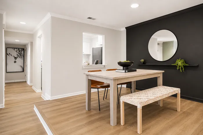 Elegant dining area with minimalist decor, featuring a stylish wooden table and bench, accented by a striking black wall with modern art.