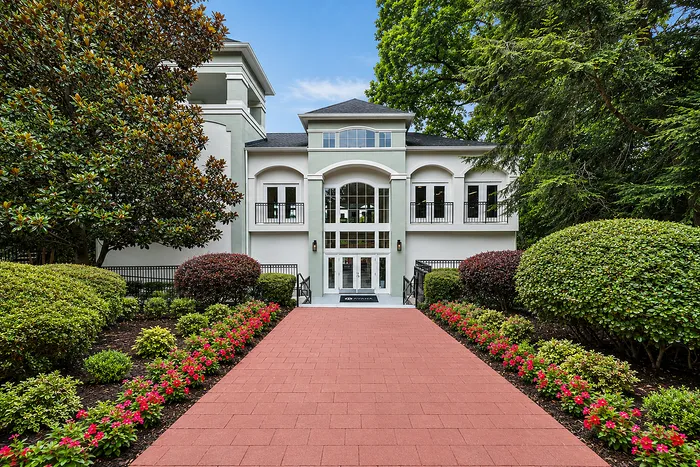 Elegant apartment entrance framed by lush greenery and vibrant flower beds, leading to a sophisticated building facade with large windows and balconies.