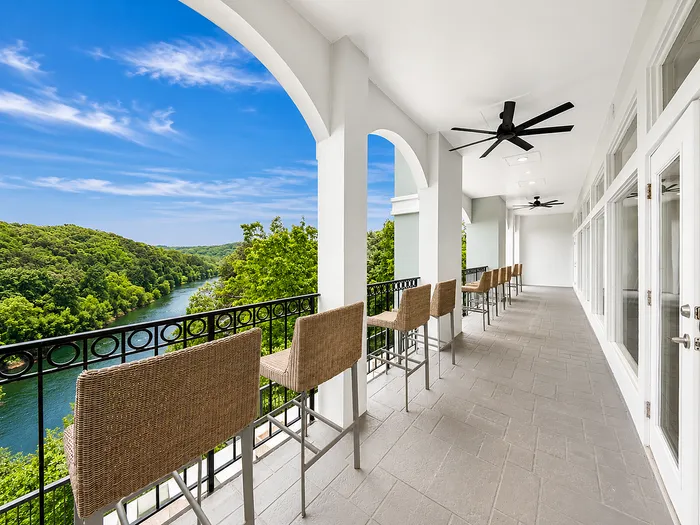 Luxurious balcony with breathtaking river and lush green hill views, featuring stylish wicker chairs and ceiling fans for a relaxing outdoor experience.