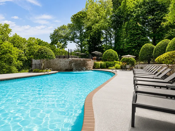 Luxurious outdoor pool surrounded by lush greenery and elegant lounge chairs, perfect for relaxing in a serene environment.