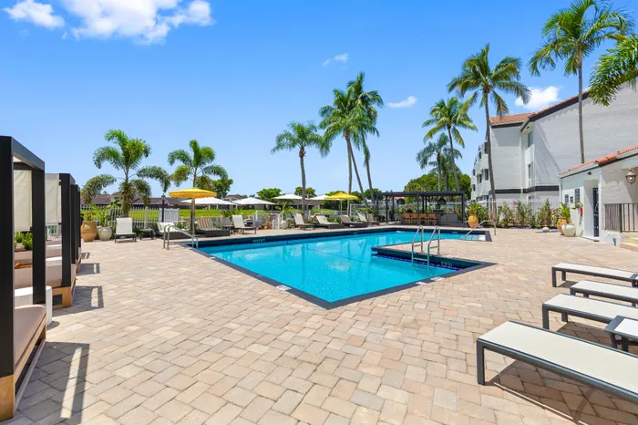 Luxurious outdoor pool area with elegant lounge chairs and tall palm trees under a bright blue sky.
