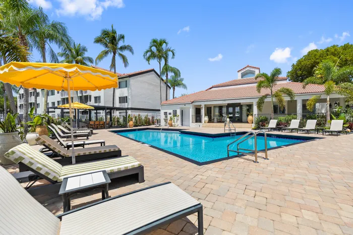 Luxurious apartment complex with a sparkling pool, elegant sun loungers, and vibrant palm trees, perfect for a relaxing tropical escape.