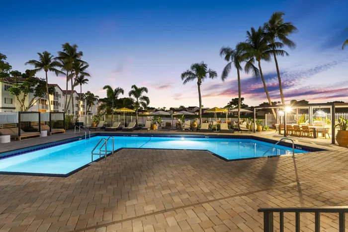 Luxurious poolside oasis with palm trees and stylish loungers, set against a vibrant sunset backdrop.