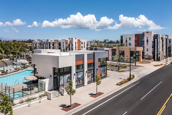 Modern apartment community with a luxurious pool, sleek architecture, and spacious living areas set against a clear blue sky.