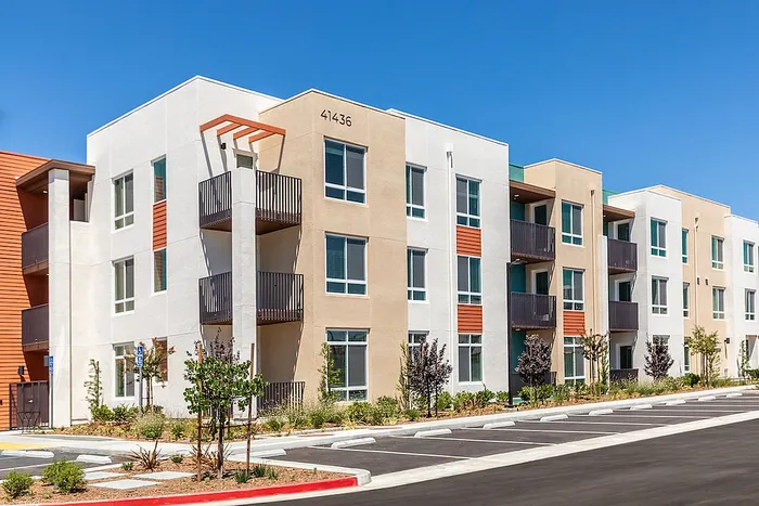 Modern apartment community with contemporary design, featuring spacious balconies and landscaped surroundings under a clear blue sky.
