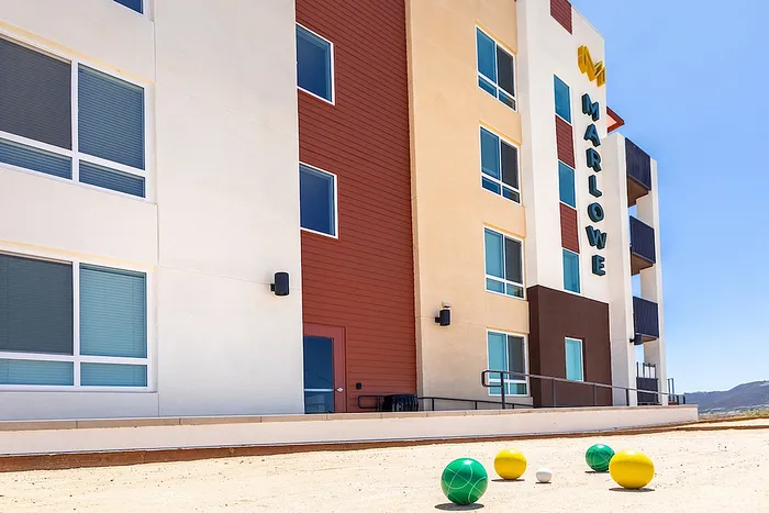 Modern apartment community with vibrant accents, clear blue-sky backdrop, and a fun outdoor bocce ball court.