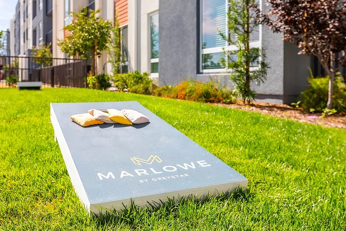 Inviting green lawn with a modern cornhole game set against contemporary apartment buildings at Marlowe by Greystar.