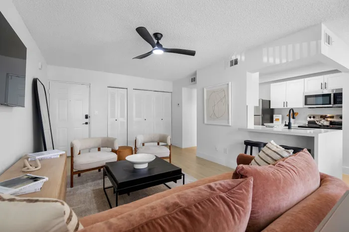 Modern and inviting living room with plush velvet sofa, contemporary chairs, sleek coffee table, and open-concept design leading to a stylish kitchen with bar seating.