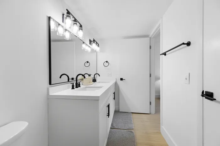 Elegant bathroom with double sinks, sleek black fixtures, and large illuminated mirror offering a modern touch.