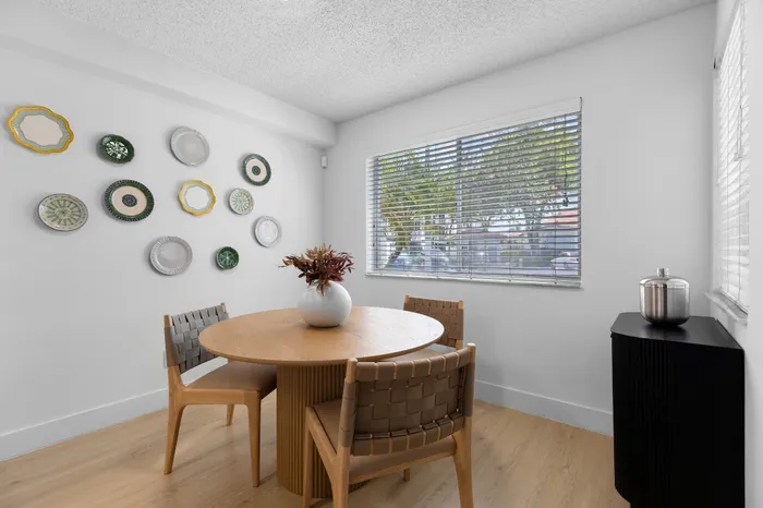 Bright and airy dining area with a modern round wooden table, elegant woven chairs, and artistic wall decor, perfect for stylish gatherings.