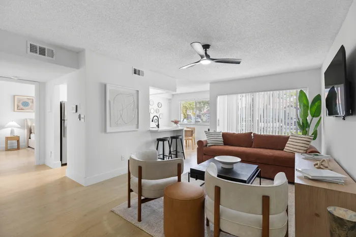 Inviting living room with modern decor, featuring a cozy sofa, stylish armchairs, and wall accents, bathed in natural light from large windows.