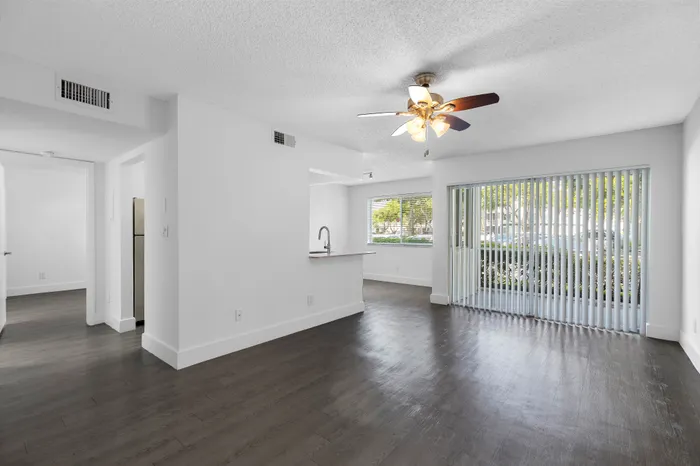 Elegant open-concept living area with dark wood flooring, natural light from large windows, and modern ceiling fan.