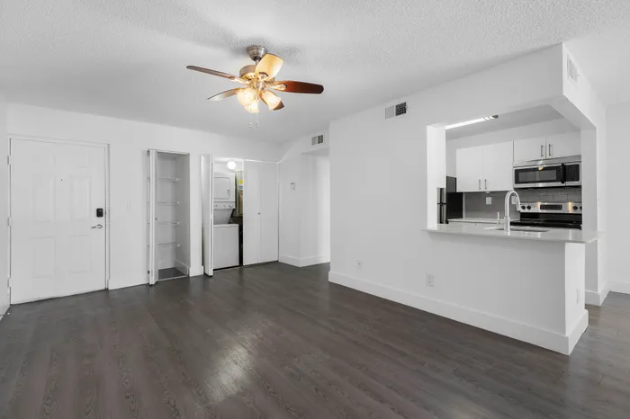 Modern apartment featuring dark wood flooring, ceiling fan, open kitchen with sleek appliances, and a convenient in-unit laundry area.