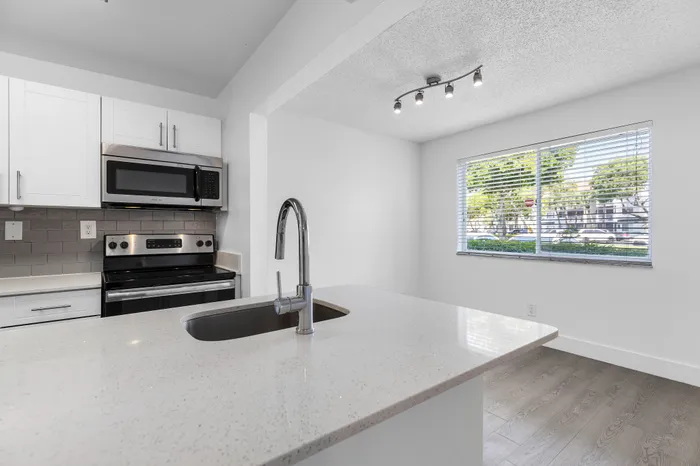 Modern kitchen with sleek quartz countertops, stainless steel appliances, and ample natural light from a large window.