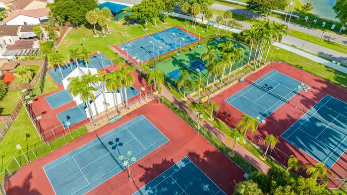 Aerial view of a vibrant sports complex featuring multiple tennis courts surrounded by lush greenery and palm trees.