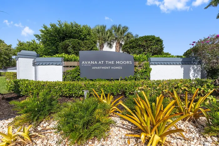 Inviting entrance sign of Avana at the Moors Apartment Homes surrounded by lush greenery and vibrant landscaping.