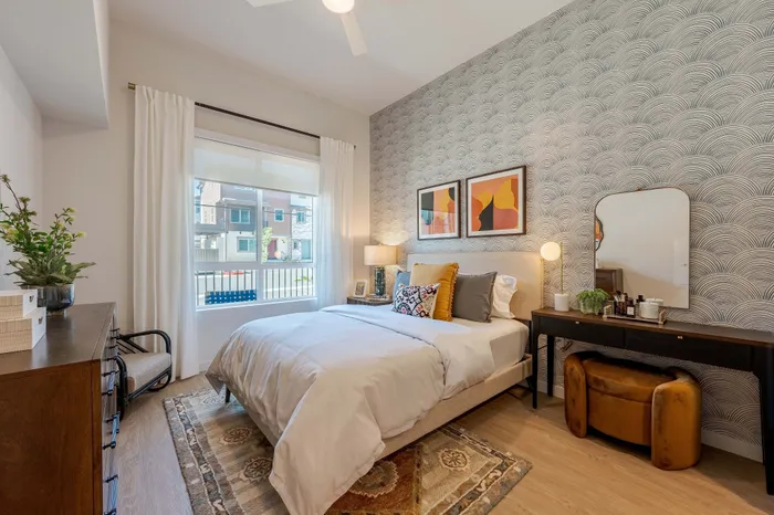 Bright and inviting bedroom with chic modern decor, featuring a comfortable bed, stylish wallpaper, and ample natural light.