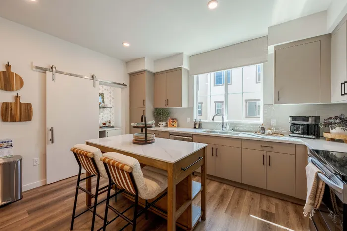 Modern kitchen with sleek cabinetry, center island with seating, and large window offering natural light.