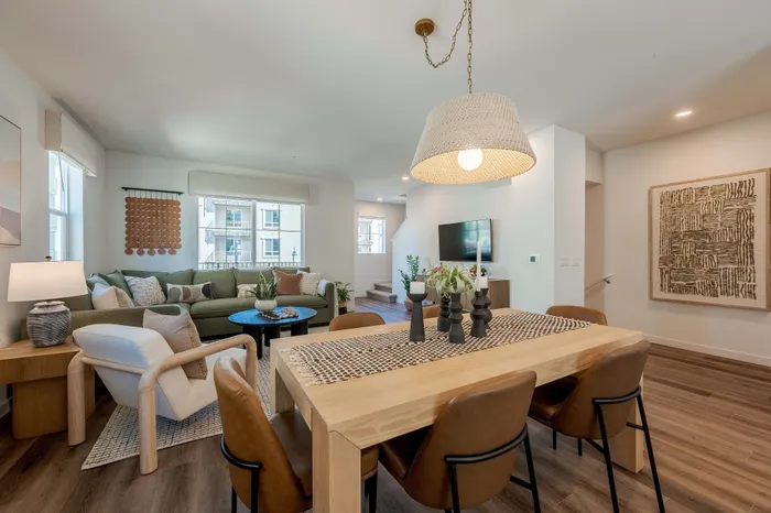 Townhome inviting open-concept living room and dining area with modern decor, cozy green sofa, and stylish pendant lighting, perfect for relaxation and entertaining.