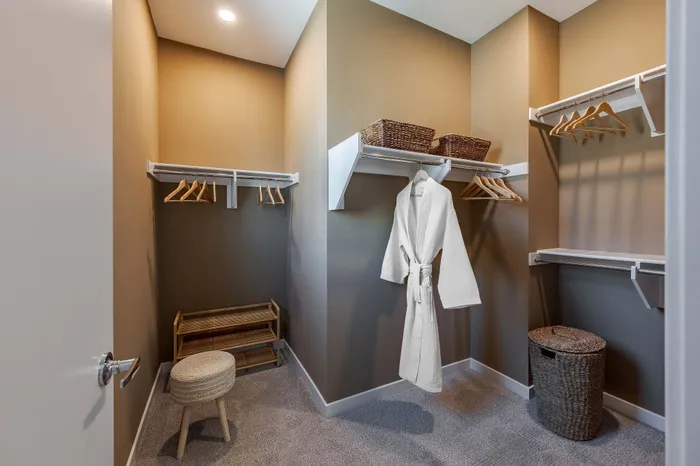 Elegant oversized closet with ample hanging space, wicker baskets, and a plush ottoman for a luxurious touch.