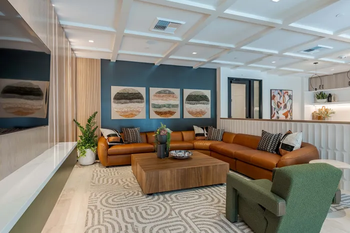 Chic club room with modern decor, featuring a stylish brown leather sectional, green armchair, and vibrant abstract art on navy accent wall.